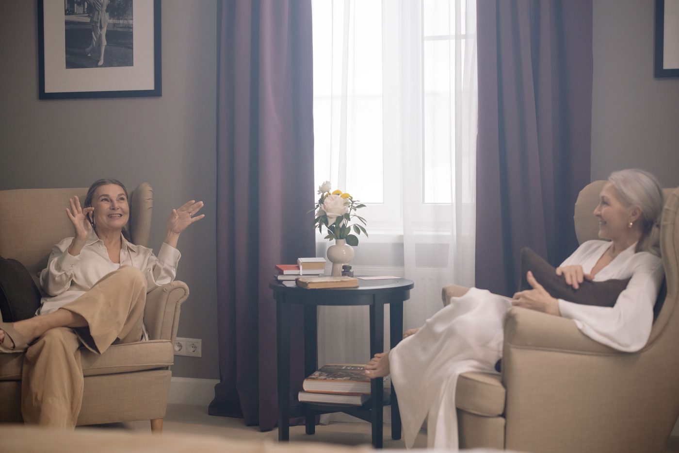 Two women relaxed in armchairs by a window, engaged in an unhurried conversation