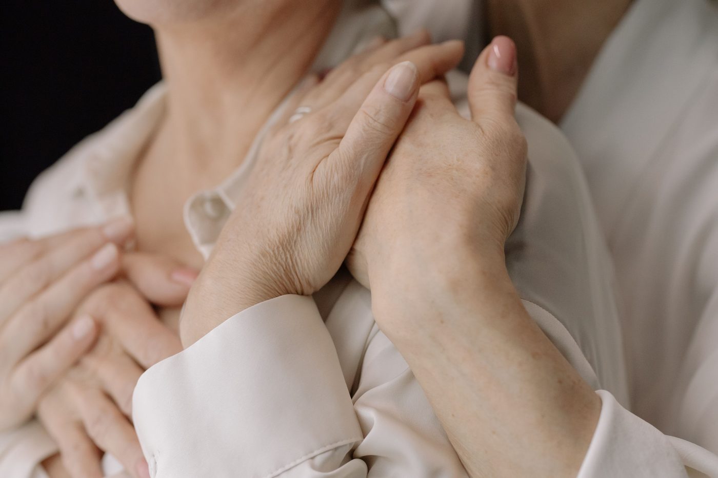 Two people's hands clasped together over a shoulder in a comforting embrace