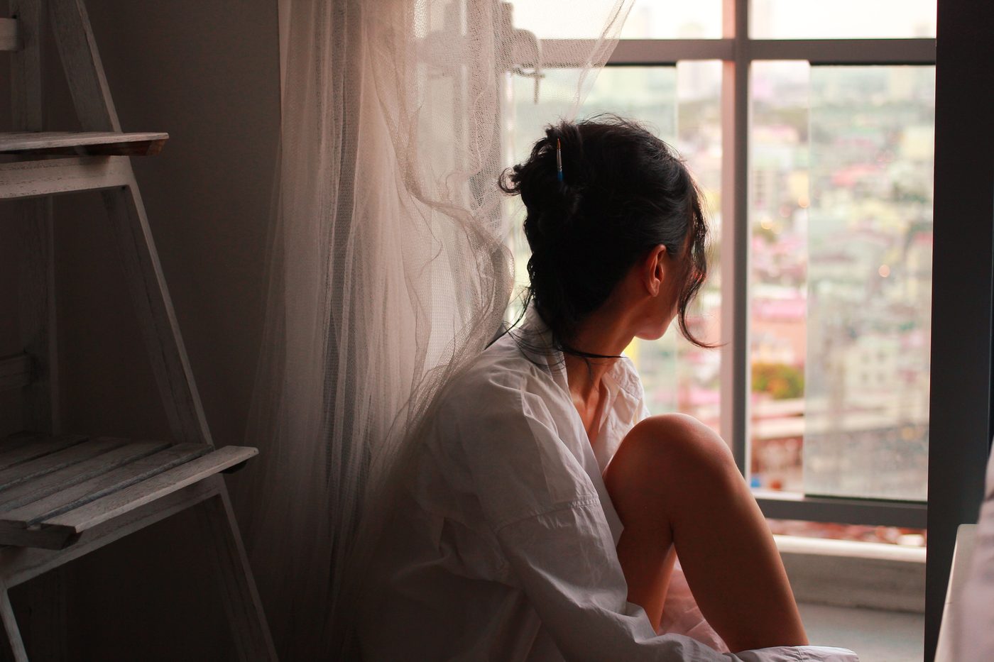 A woman seen from behind, sitting quietly and looking out a window in warm light